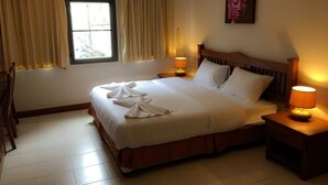 A hotel room with a large bed, two bedside lamps, a window with curtains, and a painting on the wall. - Same Same Guesthouse (Patong)