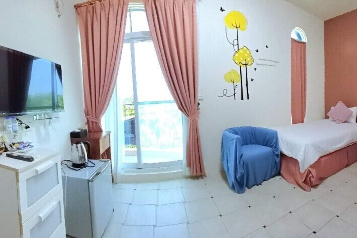 A hotel room with a bed, a desk with a computer, a TV, and a window with curtains.