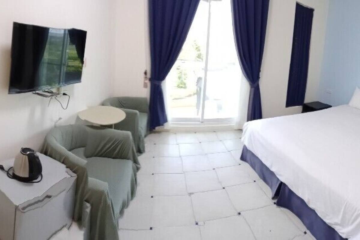 A hotel room with a bed, a desk with a chair, a television, and a window with curtains.