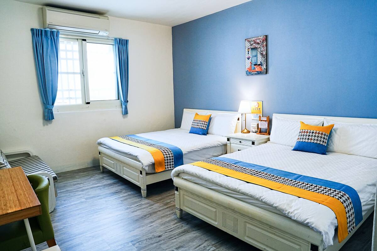 A hotel room with two beds, a desk, and a window with curtains.