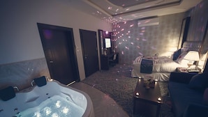 A room with a large bathtub, a sofa, a small table with candles, and a television. - Rest Night Serviced Apartments  Wadi Al Dawasir رست نايت للشقق المخدومة - وادى الدواسر (Wadi-Ad-Dawasir)