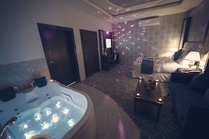 A room with a large bathtub, a sofa, a small table with candles, and a television. - Rest Night Serviced Apartments Wadi Al Dawasir رست نايت للشقق المخدومة - وادى الدواسر (Wadi-Ad-Dawasir)