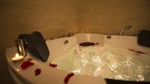 A hot tub with rose petals, a candle, and a shower head. - Rest Night Serviced Apartments  Wadi Al Dawasir رست نايت للشقق المخدومة - وادى الدواسر (Wadi-Ad-Dawasir)