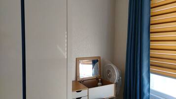 A bedroom with a wooden dresser, a mirror, a fan, and a window with blinds.