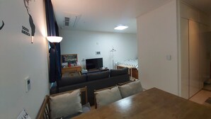 Una sala de estar con sofá, televisión, escritorio y mesa de comedor con sillas.