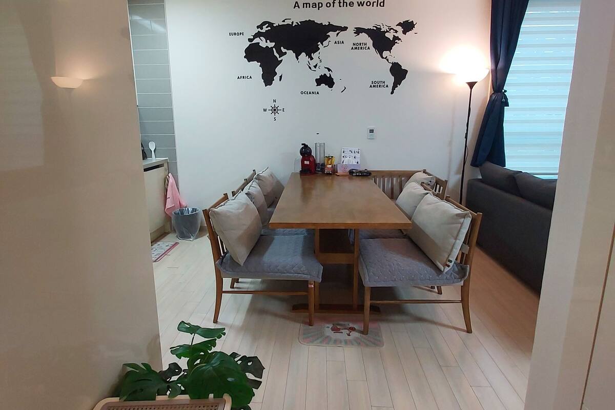 Un comedor con mesa y sillas de madera, un mapa mundial en la pared y una ventana con cortinas.
