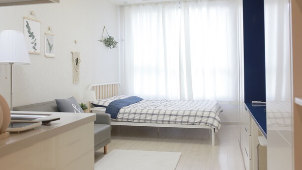 Un dormitorio con cama, escritorio, silla, lámpara y ventana con cortinas.