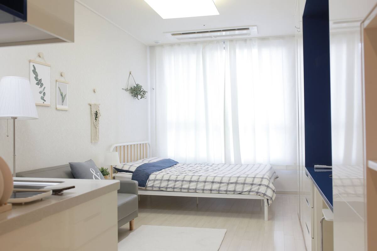 Un dormitorio con cama, escritorio, silla, lámpara y ventana con cortinas.