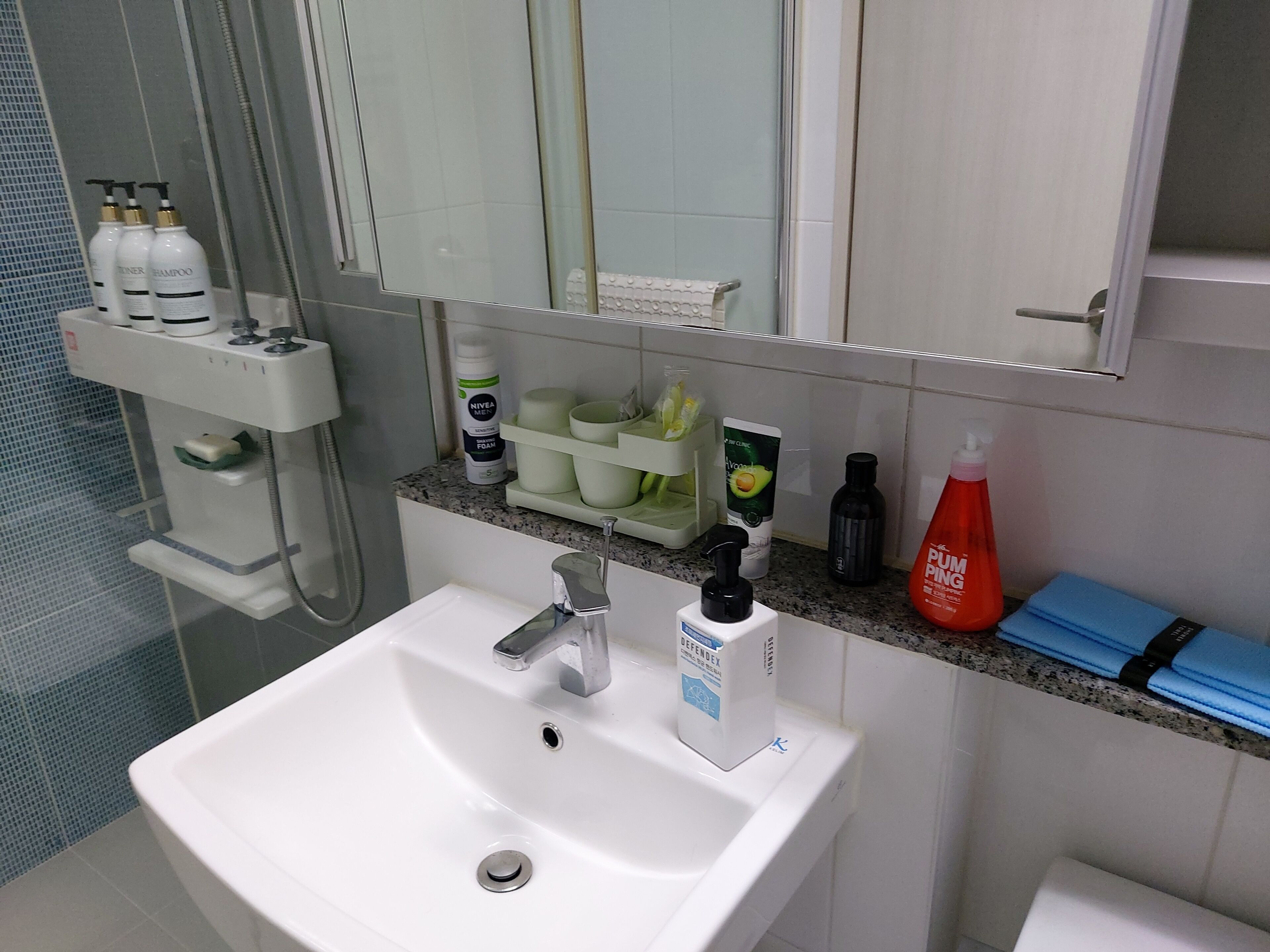 A bathroom with a white sink, a mirror, and various toiletries on the countertop.