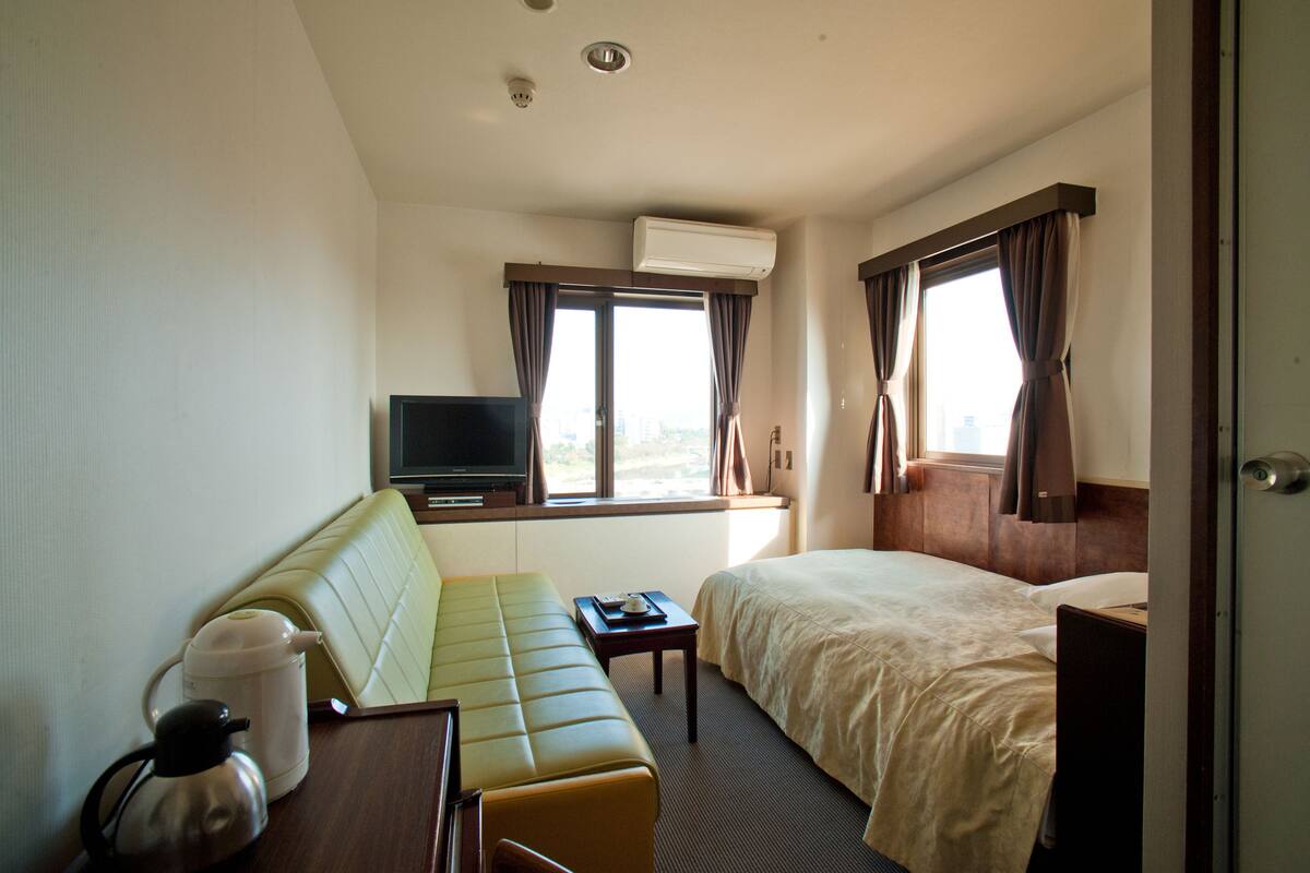 Ein Hotelzimmer mit Bett, einer Couch, einem Fernseher und einem fenster mit Vorhängen.