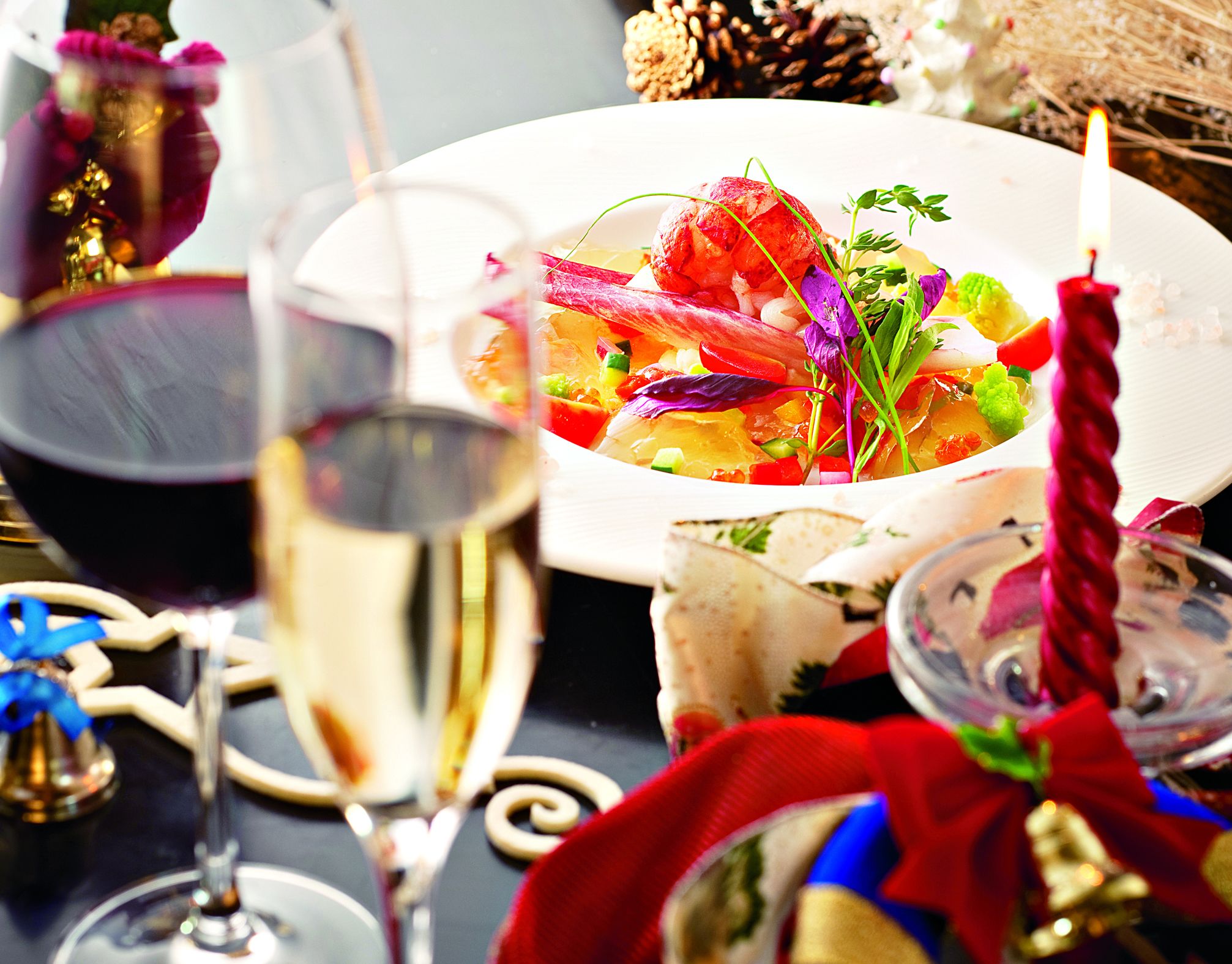A festive table setting with a plate of food, glasses of wine, and decorative elements like a candle and a Christmas ornament.