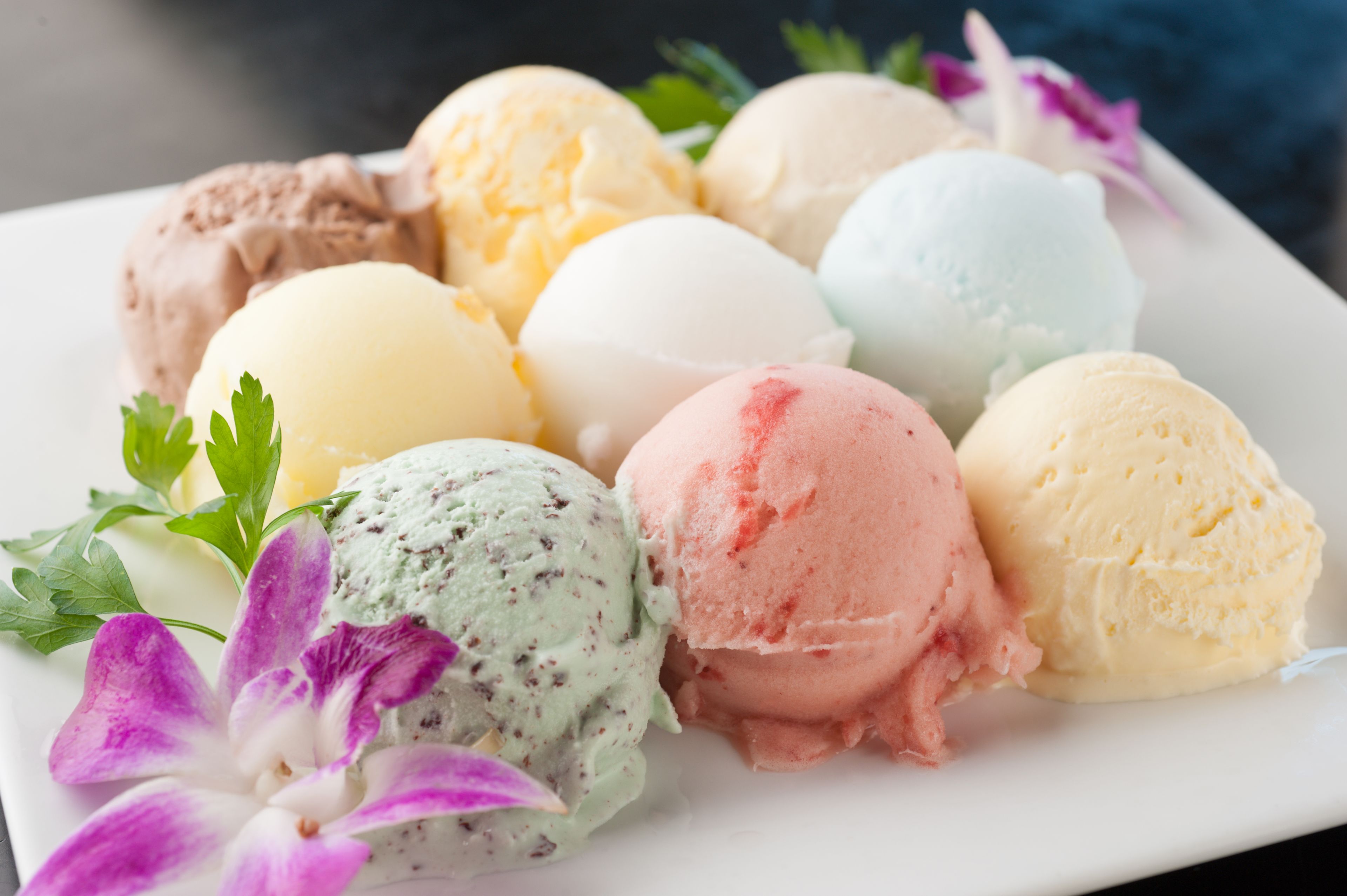 A plate of assorted ice cream flavors garnished with green leaves and purple flowers.