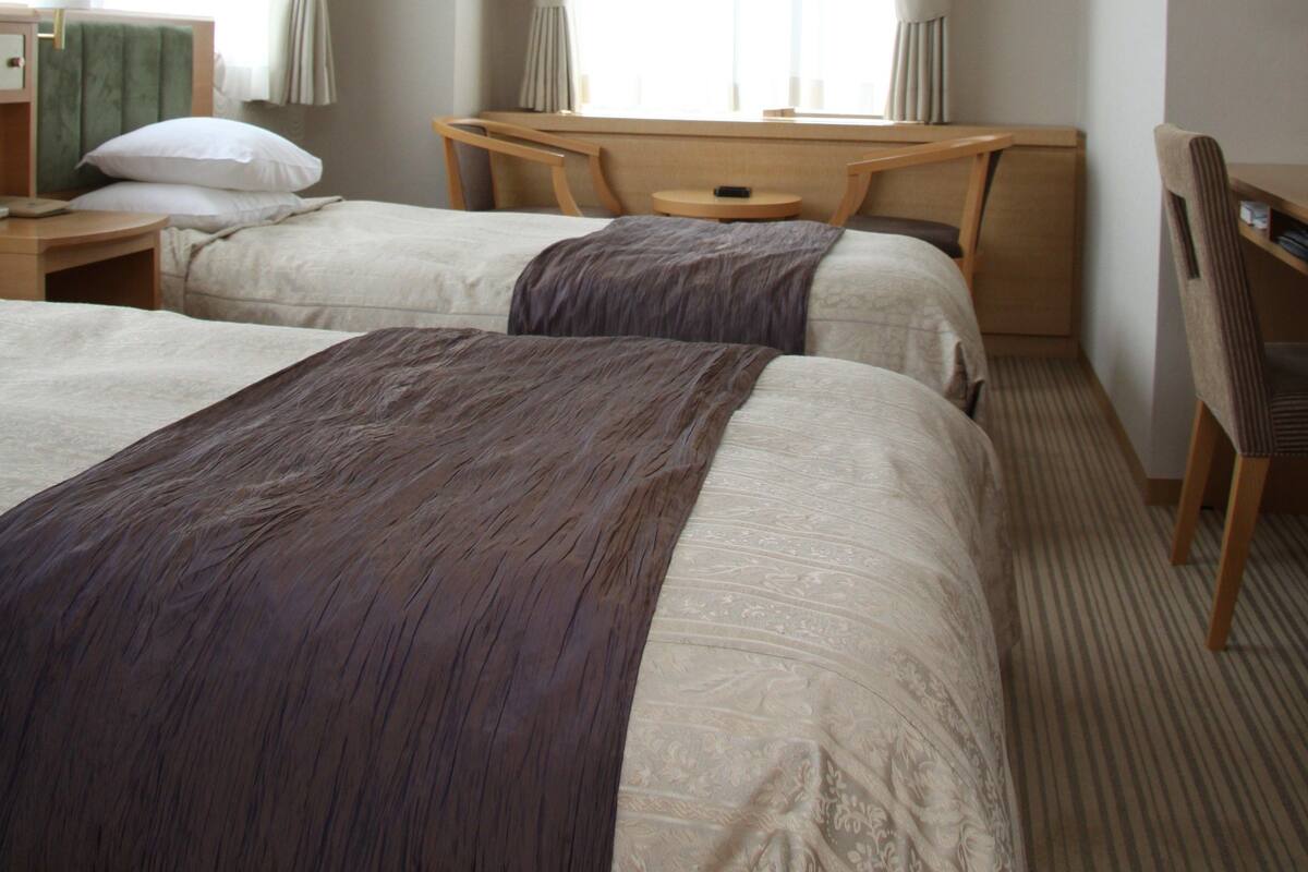 Ein Hotelzimmer mit zwei Betten, einem Schreibtisch und einer Klimaanlage.