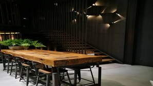 A modern dining area with a long wooden table, metal chairs, and a staircase. - Sook Station (Bangkok)