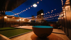 An outdoor pool area with string lights, a wooden deck, and a building with large windows. - Sook Station (Bangkok)