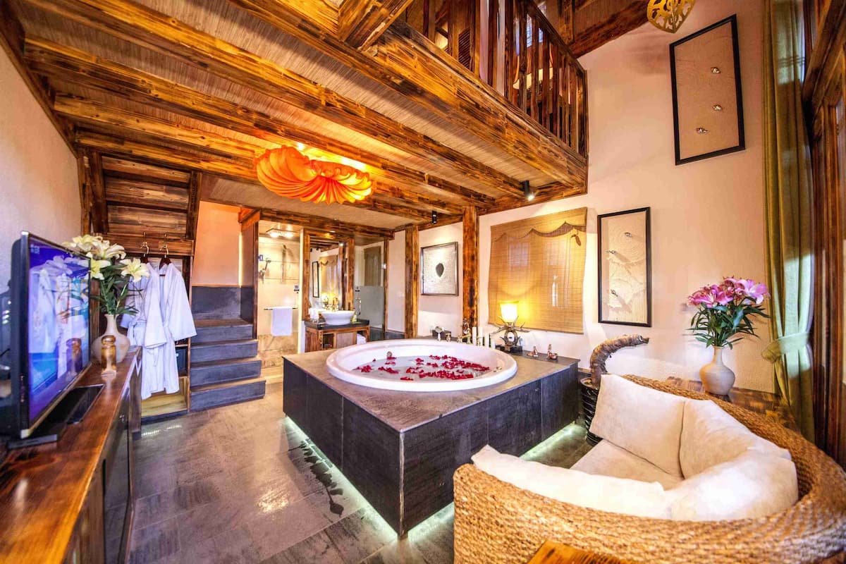 A luxurious bathroom with a large bathtub, wooden ceiling, and a wicker sofa.