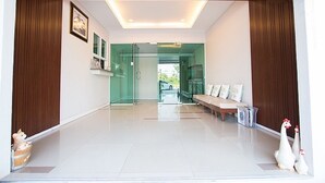 A modern hotel lobby with a glass door entrance, a bench, and a white rooster statue. - Krit Place (Nonthaburi)