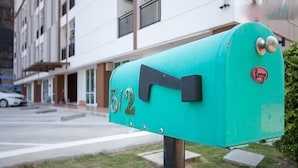 Ein türkisner Briefkasten mit der Nummer 512, gelegen auf einem Bürgersteig vor einem Gebäude.