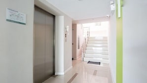 Ein Korridor mit einem Metallaufzug, einer Treppe und einer Wand in Grüntönen.