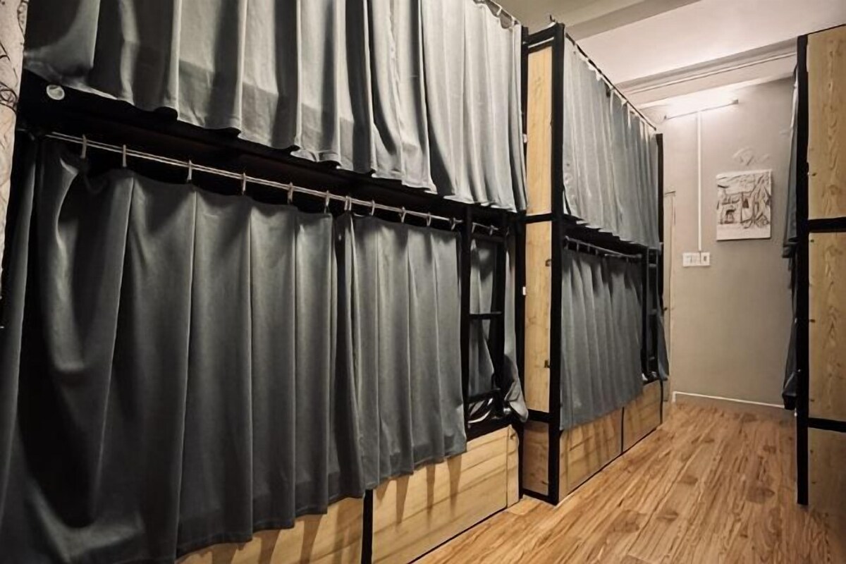 Una stanza con pavimento in legno, un letto dalla struttura nera e un'asta per tende grigie fissata alla parete.