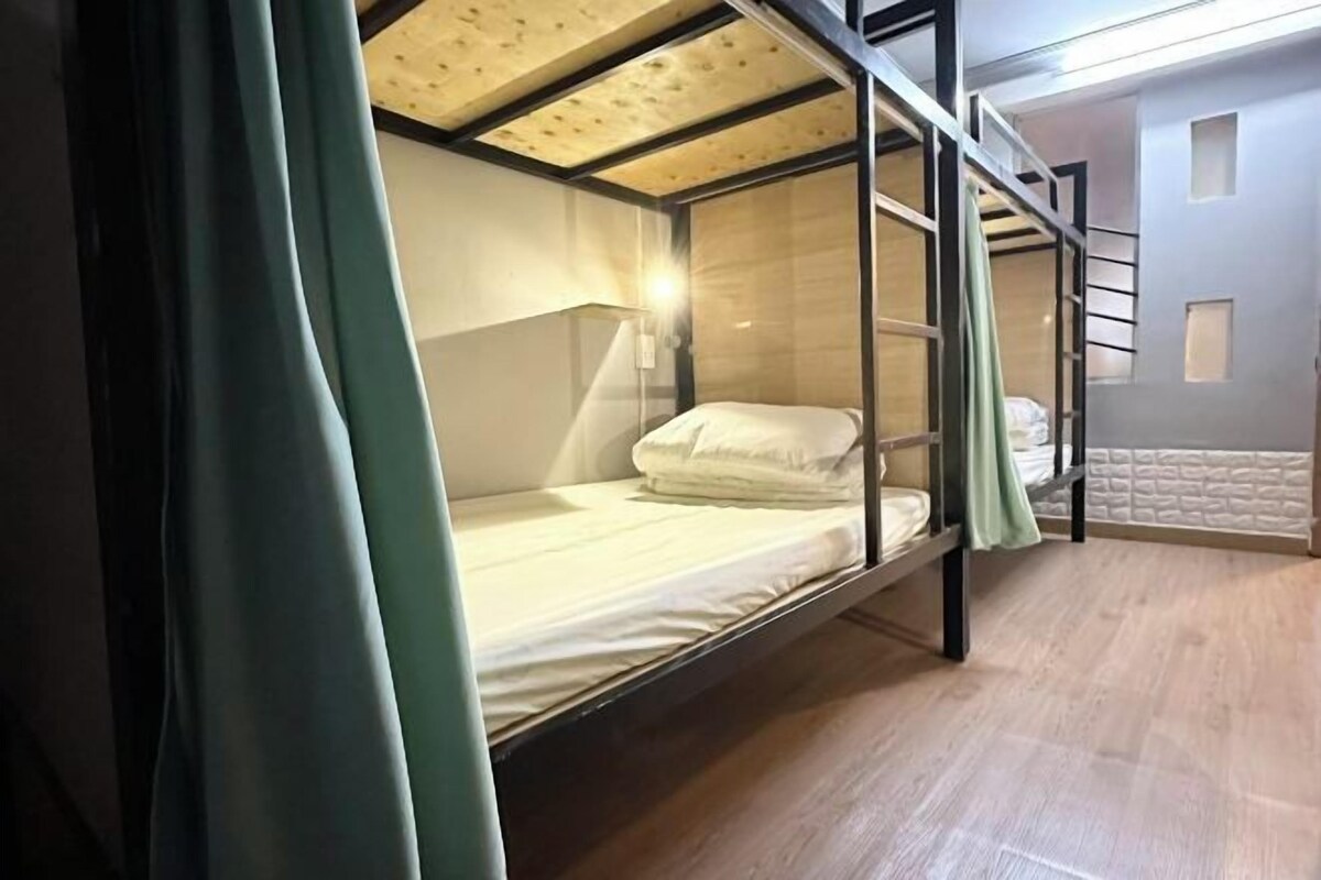 Camera con letto a castello, soffitto in legno, un letto singolo con biancheria bianca e una tenda verde.