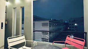 A balcony with two chairs and a table, a railing, and a view of buildings at night. - Alleyway Hostel - Adults Only (Ho Chi Minh City)