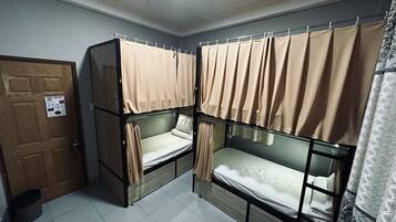 A dormitory room with bunk beds, a wooden door, and a tiled floor.