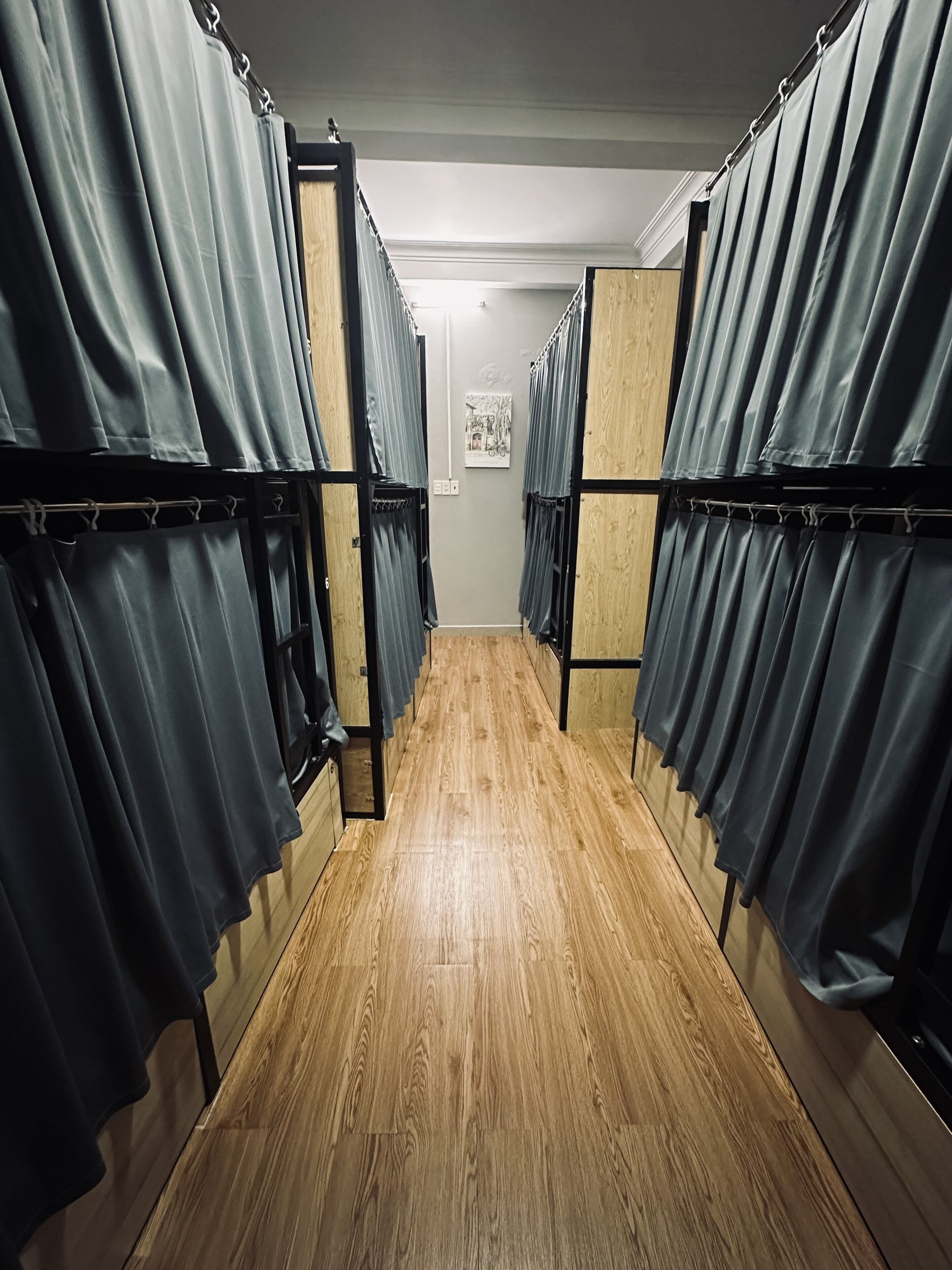 Un couloir bordé de pièces séparées par des rideaux, avec un plancher en bois et un tableau encadré accroché au mur.