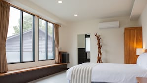Un dormitorio con un ventanal grande, una cama, una mesita de noche de madera, un espejo y un aire acondicionado.