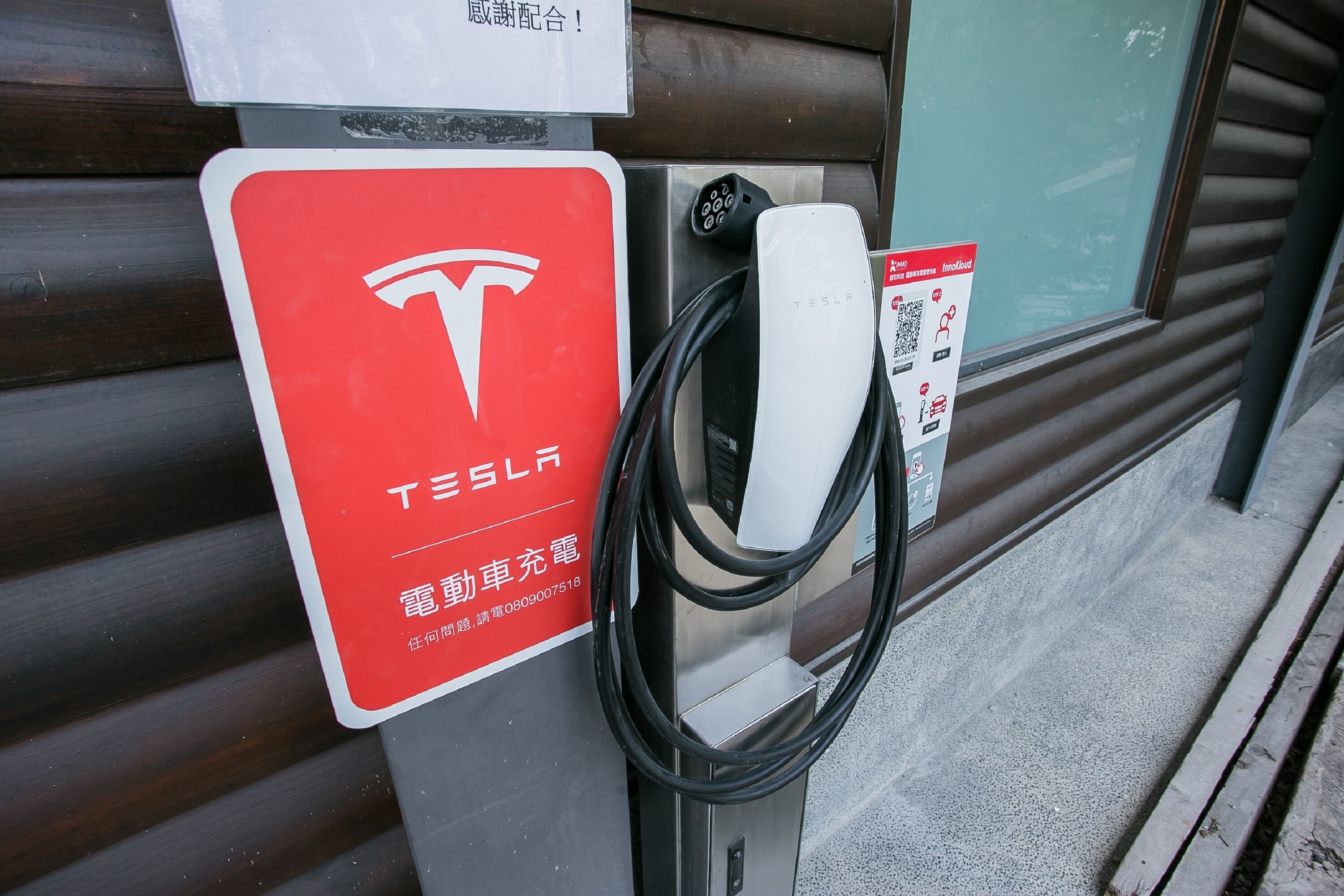Eine Tesla Ladestation mit einem roten Schild und einem QR-Code.