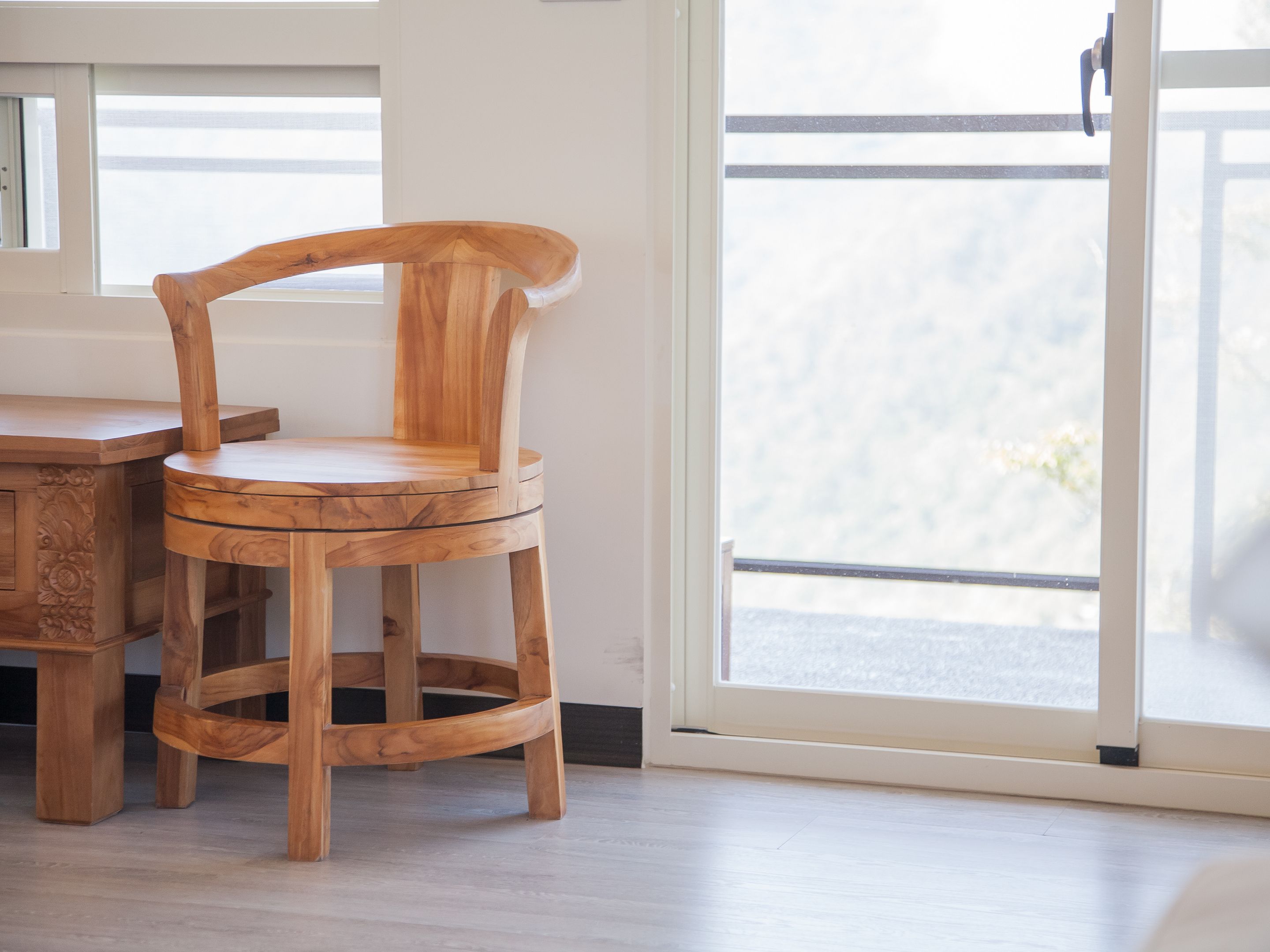 A wooden chair with a curved backrest and a round seat, positioned next to a wooden table with a glass top.