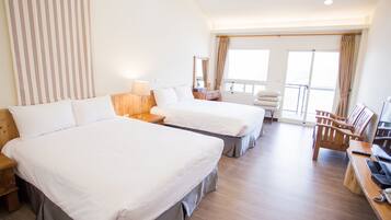 A hotel room with two beds, a desk with a computer, a chair, and a balcony with curtains.