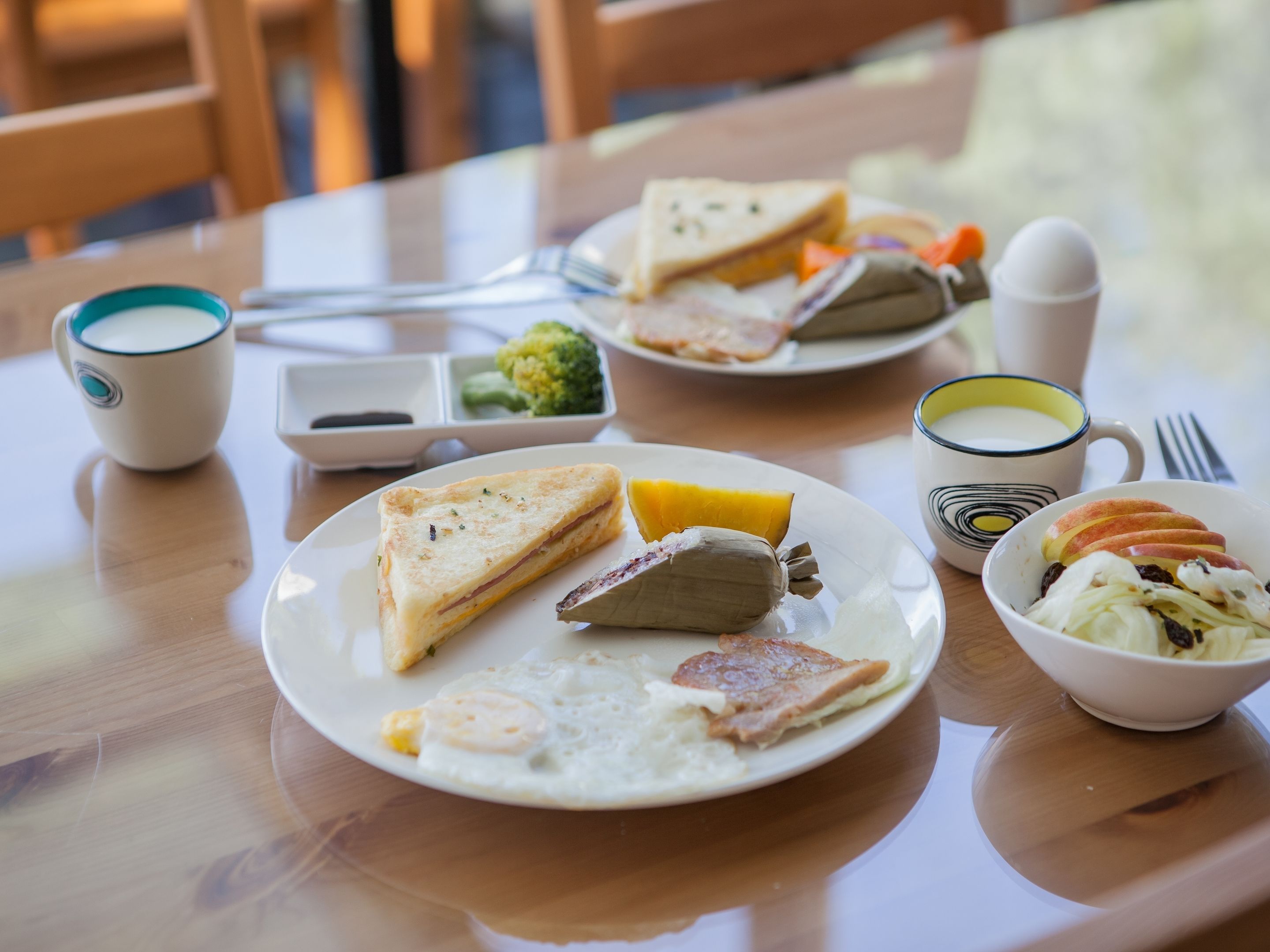 Ein Tisch mit einem Teller Essen, darunter Toast, Eier und einem in Folie gewickelten Gegenstand, eine Salatschüssel und eine Tasse.