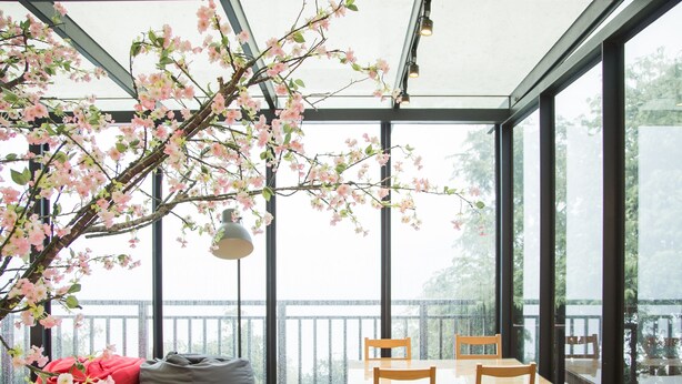 Un interior moderno con una mesa y sillas de madera, un banco con cojines y un ventanal con vistas a un balcón.