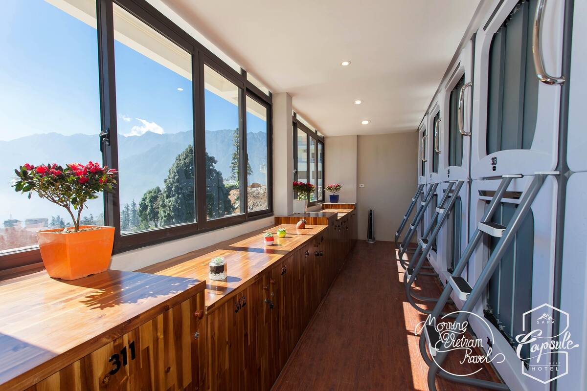 A hotel corridor with wooden paneling, large windows offering mountain views, and a long counter with potted plants.