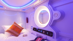 Una habitación de hotel moderna con una cama, un panel de control, un espejo circular y una botella de agua en la mesita de noche.