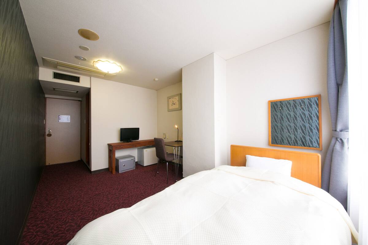 A hotel room with a bed, desk, chair, and a small TV.