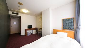 A hotel room with a bed, desk, chair, and a small TV.