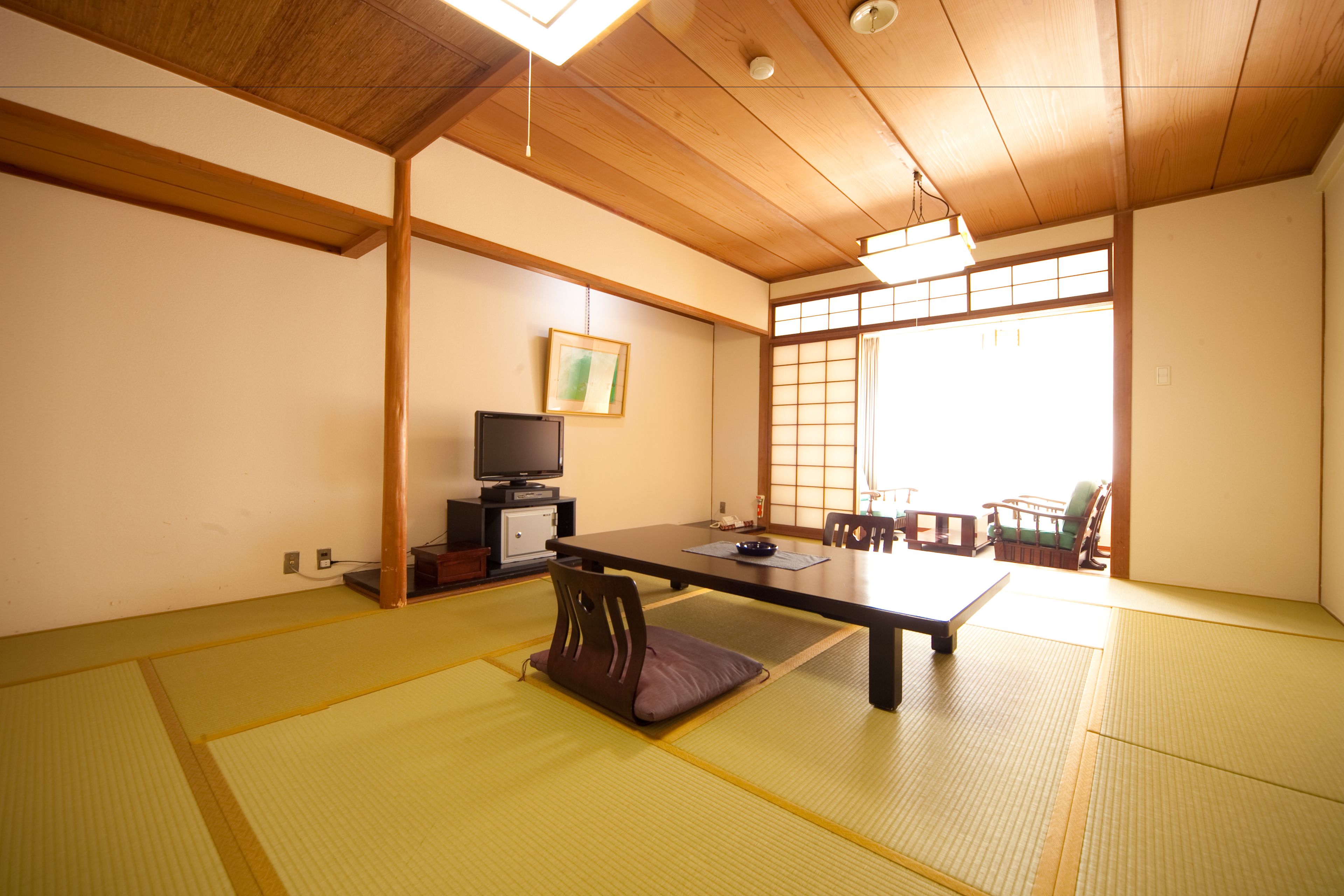 Una habitación japonesa tradicional con suelo de tatami, una mesa baja, un televisor y puertas correderas.