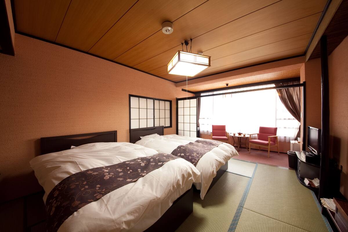 A hotel room with two beds, a tatami mat floor, a television, and a view of the outside.