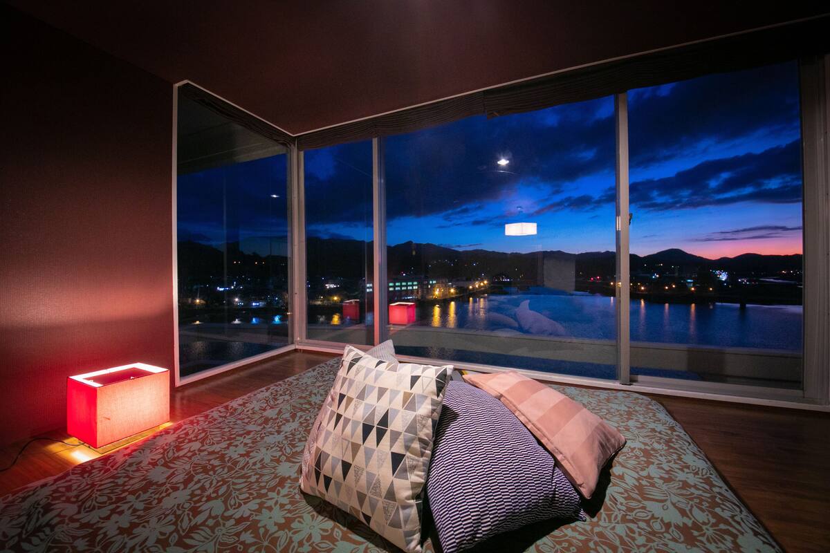 A modern room with a large window overlooking a body of water at dusk.
