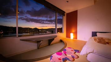 A modern hotel room with a large window, a bedside table, a bed, and a unique patterned rug.