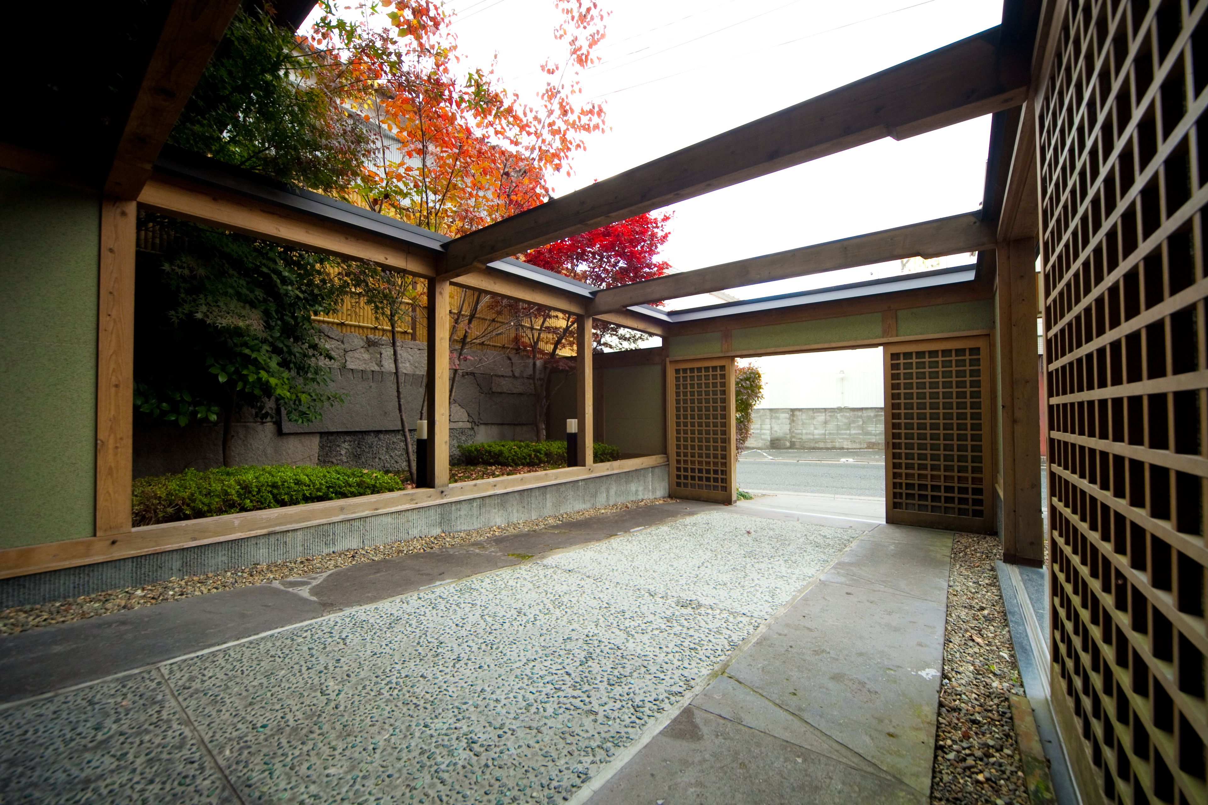 A traditional Japanese courtyard with a wooden walkway, stone flooring, and a view of autumn foliage.
