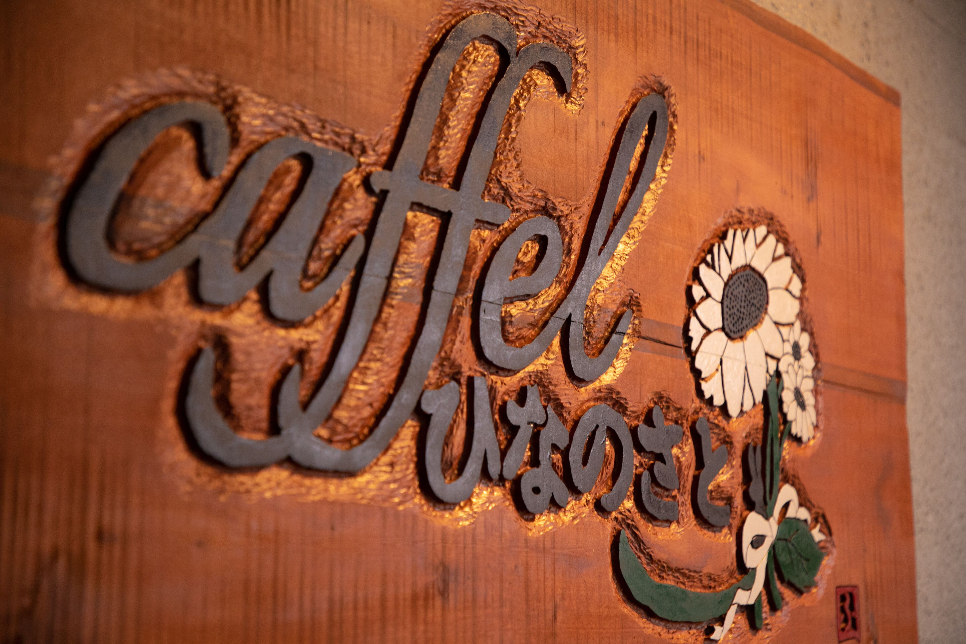 Un letrero de madera con la palabra 'cafe' y un diseño de girasol.