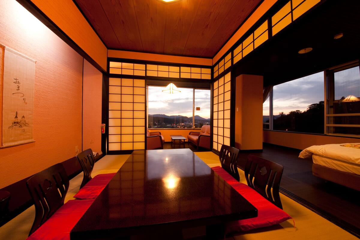 A traditional Japanese-style room with tatami mats, a wooden dining table, and a view of the cityscape through large windows.
