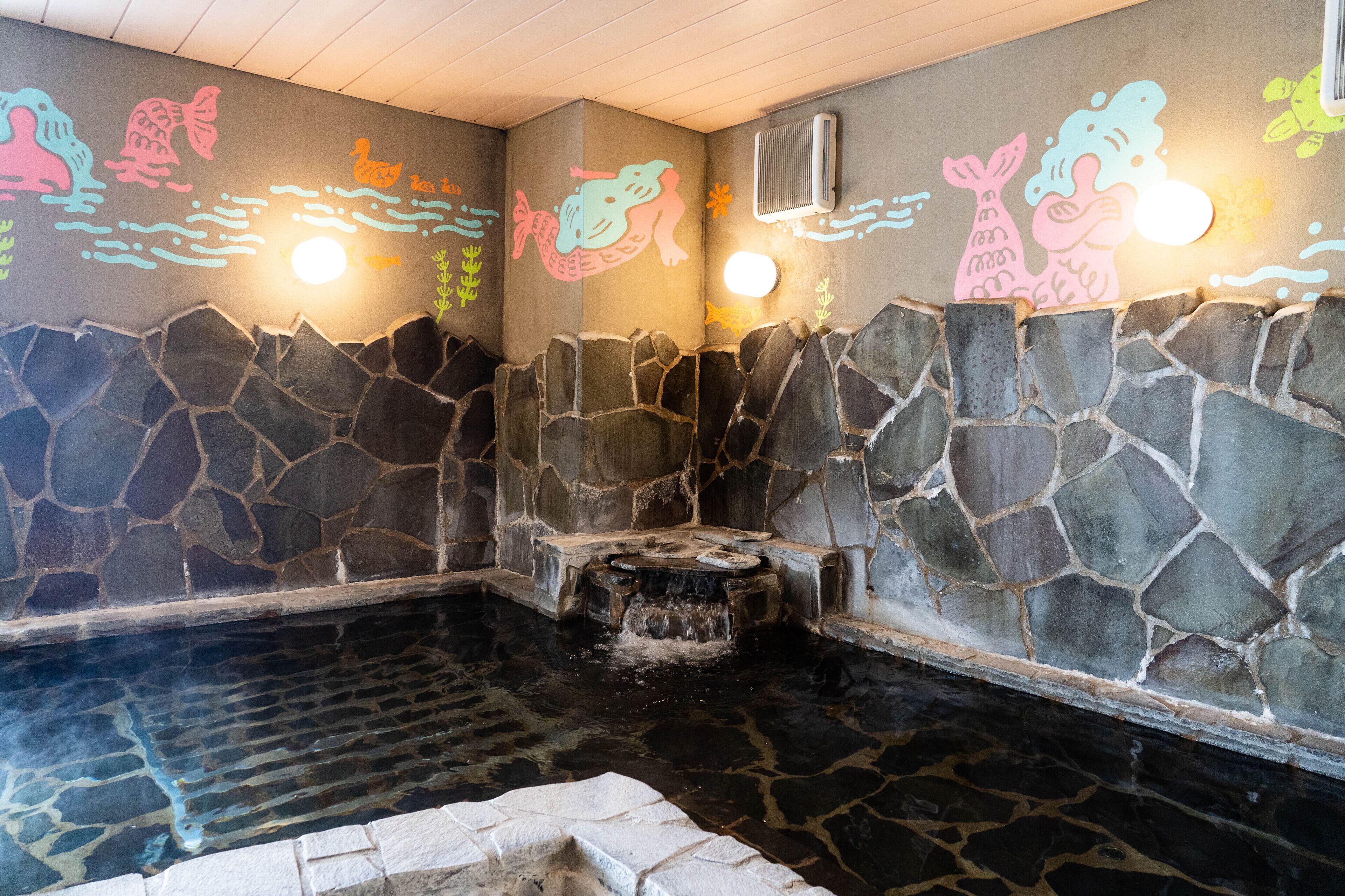 Un baño de aguas termales con paredes de piedra, ilustraciones coloridas y un banco de piedra.