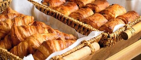 En træbakke med to fletkurve fyldt med croissanter og andet bagværk.