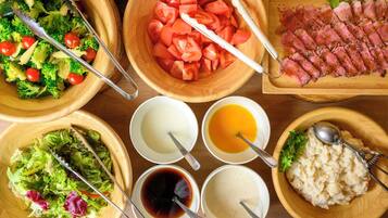 A variety of food items including a salad, sliced tomatoes, ham, and different sauces in wooden bowls.