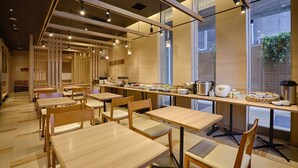 A modern dining area with wooden tables and chairs, a long counter with kitchen appliances, and large windows allowing natural light. - Hotel Forza Hakataeki Chikushi - GuchiⅠ (Fukuoka)