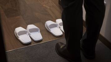 A wooden floor leading to a carpeted area with white slippers placed on it.